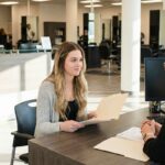 A prospective student with a folder discusses enrollment requirements with an admissions officer in a beauty school lobby.