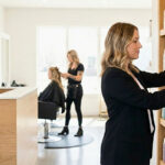 A woman working in salon retail management and a receptionist at the front desk, illustrating beauty jobs that do not require a license alongside licensed hair services in the background.